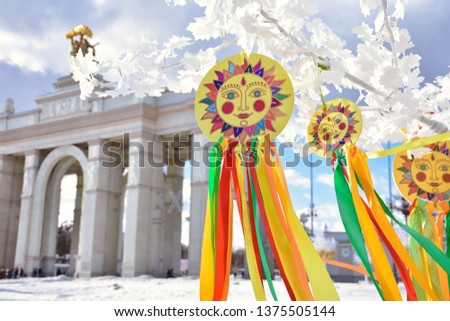 emblem of sun with colorful ribbons on branches of white tree,multi-colored ribbons against stone building,sun picture,Shrovetide in park,images of sun with ribbons at Shrovetidel,Pancake week Royalty-Free Stock Photo #1375505144