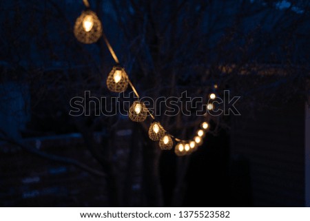 Patio lights in a backyard strung between a house and a garage at night 