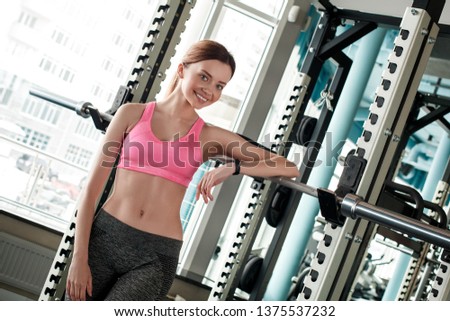 Young woman in gym healthy lifestyle standing leaning on trainer looking camera smiling happy