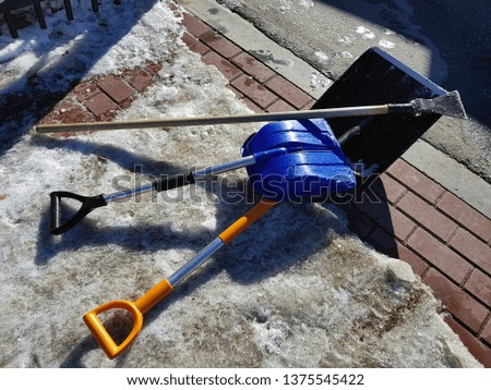 Beautiful snow shovel and ice ax in the snow against the background of a tile and fence in spring or winter