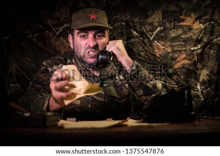 The evil dictator sitting on table. Angry communist general sitting at headquarter or Cuban commander in dark room. Studio decoration