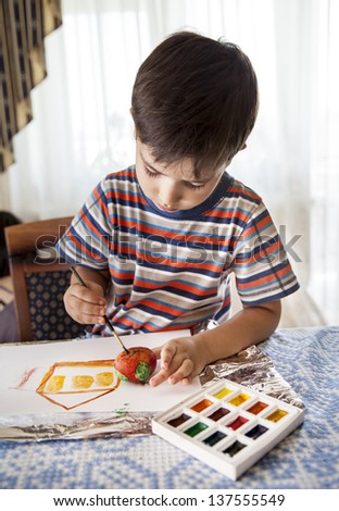 Home and family. Little boy draws house and easter egg with watercolor