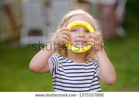 Cute toddler girl outdoors portrait in summer day. Smiling and charming child. Kid playing in game throwing rings at summer outdoors.
