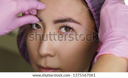 Microbleeding and eyebrow architecture. Beautician forms lines of symmetry on girl's face. Cosmetic procedure in spa salon. Face beauty.