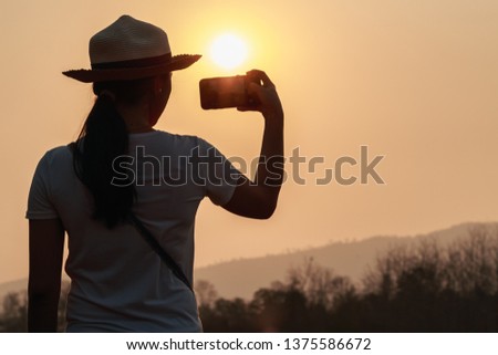 Asian teen woman holding Smartphone wearing a hat at Sunset