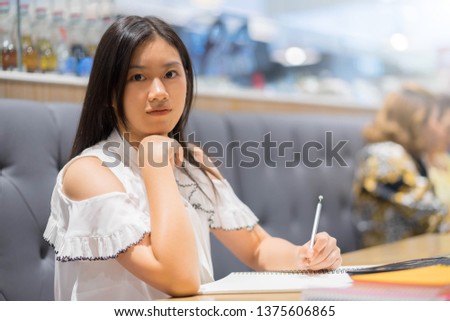 Portrait of young asian female student writing in a book at a table in a cafe.Background in cafe.