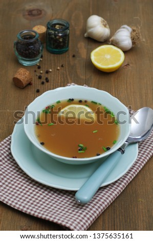Bone broth in a bowl, lemon, garlic and peppercorns on background