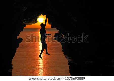 Man climbing in the cave by the sea with red sky and sunset background