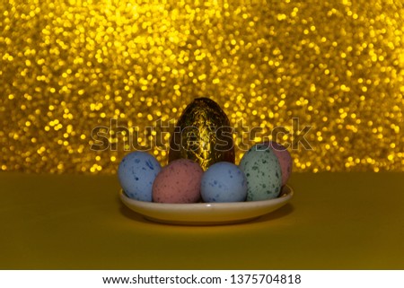 Golden egg on a golden background with defined bokeh, surrounded of colorful eggs