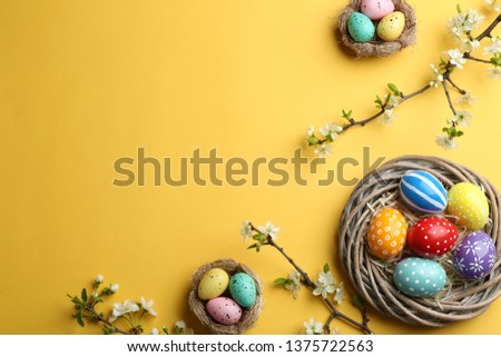 Flat lay composition with painted Easter eggs and blossoming branches on color background, space for text