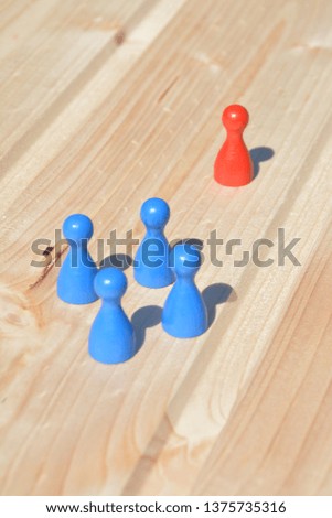 A single character faces a group of figures, all throwing a shadow in the same direction on a bright wooden surface - a concept of the conflict between a single and a group