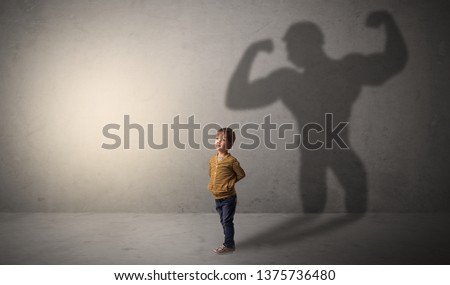 Little waggish boy in an empty room with musclemen shadow behind