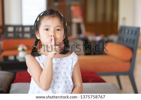 Asian child cute or kid girl squat and forefinger close mouth for tell quietly shh or stop silence and secret surprise with play hide and seek in library room at school or reception room Royalty-Free Stock Photo #1375758767