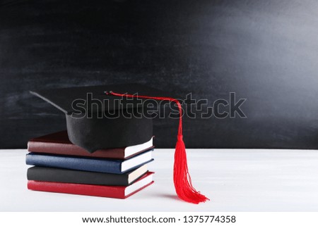 Graduation cap with stack of books on white wooden table