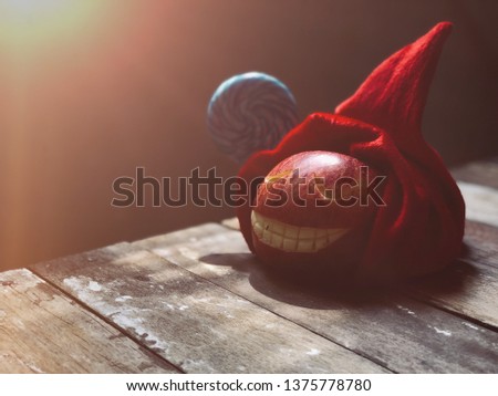 Red Apple fruit,carved with smiling face like the pumpkin smile in halloween festival,on red christmas hat like a Santa Claus,on old wood plank,rustic still life and dark background.Halloween concept.