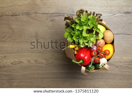 Paper bag full of fresh vegetables on wooden background, top view. Space for text