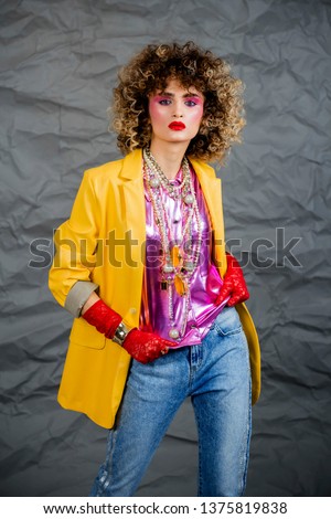 
Portrait of a girl in a yellow jacket and blue jeans with afro hair of the eighties, disco era. Photo in studio on a gray background.