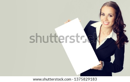 Happy smiling woman in black confident clothing showing blank signboard with copyspace empty area for some text or slogan, over grey background. Business and advertising concept photo.