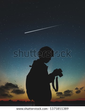 Silhouette of photographer standing in nature background with shooting star and night sky.