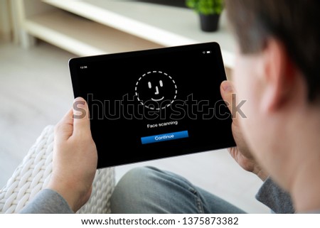 man hands holding computer tablet with face ID scanning on the screen in home room