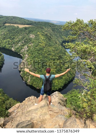 A mas who is staying on rock the and looking to river and nice scenery in the middle of forest in the Czech republic. Young and happy traveller is enjoying nice moment. Viewpoint and beautiful woods