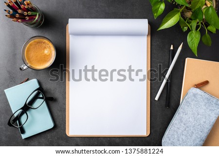 Design concept - top view of white A4 flipped paper with brown clipboard, potted plant, glasses, coffee, pencil caes on black background for mockup. real photo, not 3D render Royalty-Free Stock Photo #1375881224