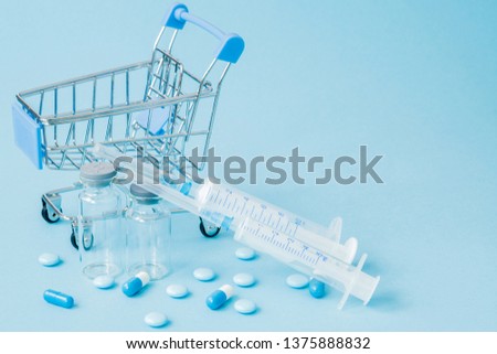 Pills and medical injection in shopping trolley on blue background. Creative idea for health care cost, drugstore, health insurance and pharmaceutical company business concept. Copy space.