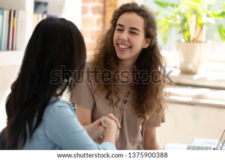 Two girl sitting at table holding hands make handclasp shaking hands, new workers greeting each other, students girls starting learn together prepare project get acquainted or concept of job interview Royalty-Free Stock Photo #1375900388