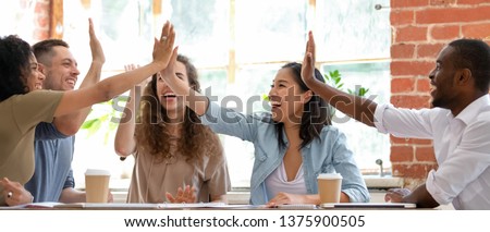 Wide horizontal image multicultural cheerful businesspeople sitting together at meeting giving high five gesture feels excited happy, showing team spirit, celebrating victory goal achievement concept Royalty-Free Stock Photo #1375900505