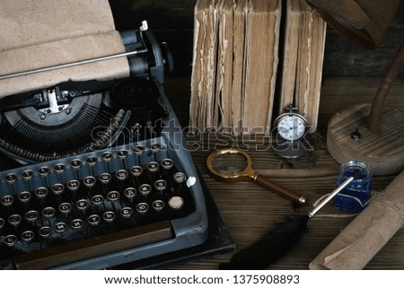 Typewriter, old books and a quill pen with a inkwell on an author desk table background.