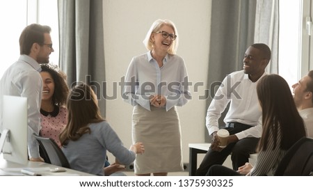 Laughing old coach team leader talking with diverse coworkers chatting at business meeting, friendly multi racial office workers and middle aged woman ceo have fun conversation at coffee break concept Royalty-Free Stock Photo #1375930325