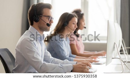 Service phone operators use headset and computer, focus on man side view answers incoming telephone calls directing to appropriate department, takes messages from clients, assistance distantly concept Royalty-Free Stock Photo #1375930358