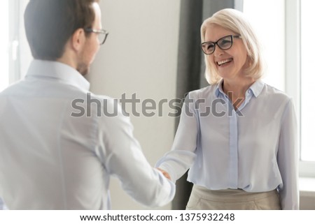 Laughing middle aged lady in glasses standing in office handshake with new employee specialist starting career at company, ceo woman welcome client shake hands express regard, nice to meet you concept Royalty-Free Stock Photo #1375932248