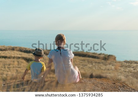 Woman and son are sitting together on the grass near the sea. Relationship mom and son concept.