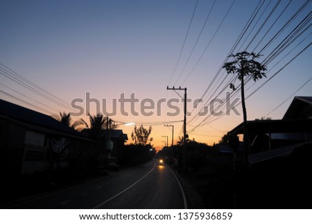 Sunrise in the far away hometown of local life. Silhouetted house and environment are simple and dark in early morning and the light of motorcycle on the road.