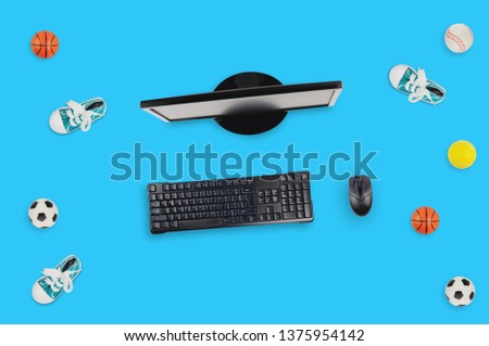 Black monitor, wireless keyboard and mouse near gumshoes and different balls on blue table. Top view. Betting concept