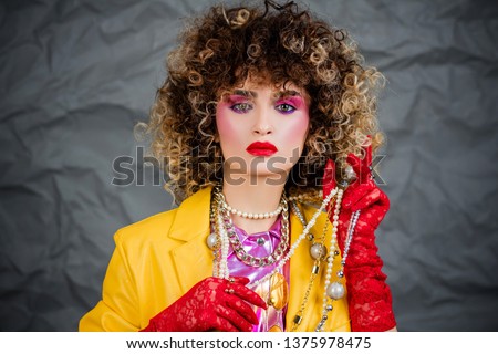 Portrait of a girl in a yellow jacket and blue jeans with afro hair of the eighties, disco era. Photo in studio on a gray background.
 Royalty-Free Stock Photo #1375978475