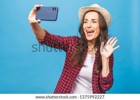 Travel concept! Charming young woman in white hat travel and take selfie on front camera smartphone isolated on blue background.