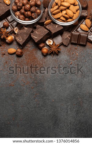 Heap of broken chocolate pieces and nuts on dark concrete background