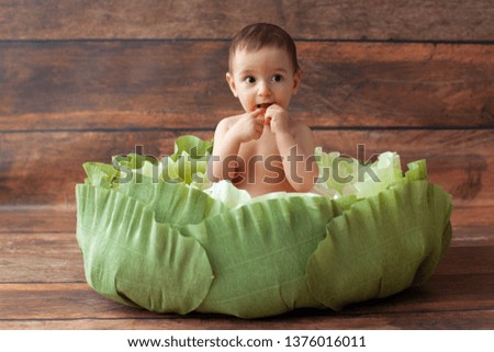 One year old boy sitting in handmade paper green cabbage. Paper art and cut. On wooden background. 
