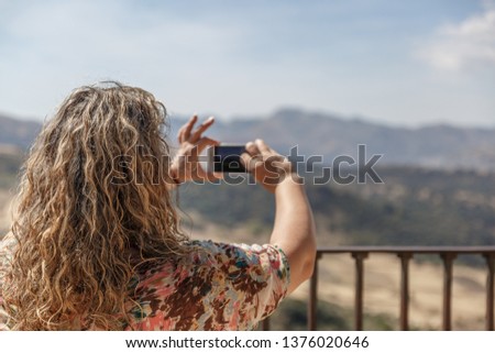 A mature woman tourist is taking a picture of a beautiful landscape in the background