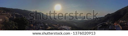 Panaromic view over the city of Jiufen in Taiwan Residential homes and mountain scape blended together with nature. The sky consist of strong sunlight in the center.