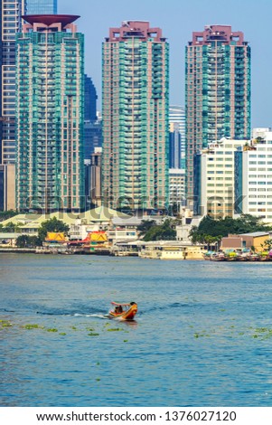 long trail boat in Chao Phraya river,  background is high rise building, condominium and hotel in business area, the blue sky in the afternoon, it's Peaceful  lifestyle in Bangkok, Thailand