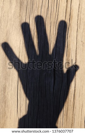 shadow of a man's hand on a wooden background. the gesture of the five fingers