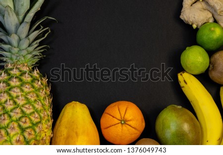 A set of fruits, fruit zarbrosani around the photo, in the middle of free space, black background, pineapple orange, banana, lime, kiwi, mango, lemon, papaya, ginger