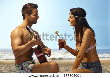 Loving couple enjoying sunset on the beach, man playing guitar, girl drinking cocktail.