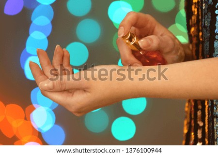 Woman spraying perfume on wrist against blurred lights, closeup