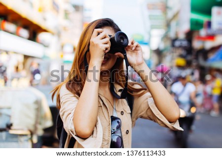 Young Asian female tourist woman holding a camera and taking photos in Bangkok, Thailand while travelling in Southeast Asia