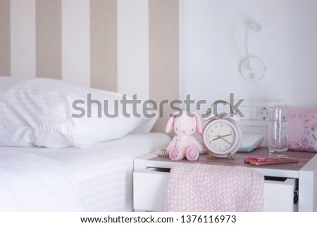 Girl's bedroom. A bed room of little girl with selective focus on the pink alarm clock next to the rabbit plush doll.