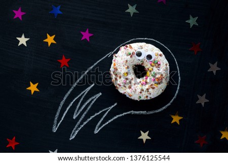 donut meteorite with googly eyes among the stars  on a black chalkboard background, funny children's entertainment with food, space concept
